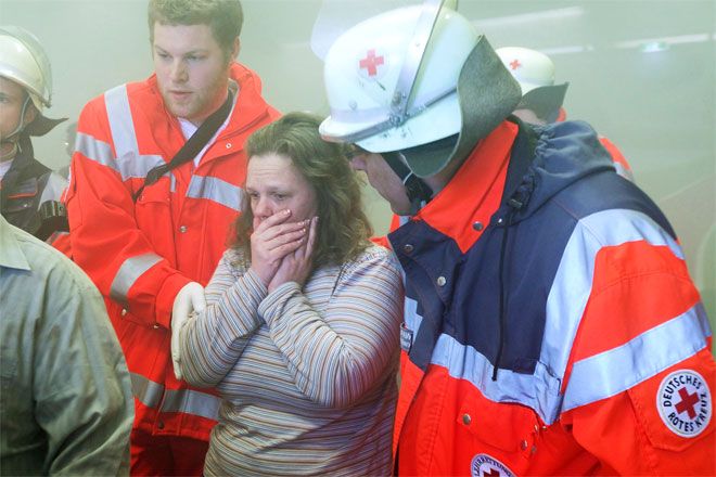 Foto: Während einer Helferübung zum Thema Brandanschlag bringen DRK-Einsatzkräfte eine Patientin aus der Gefahrenzone. Es liegt Rauch in der Luft, die Patientin hält sich ihre Hände vor den Mund.