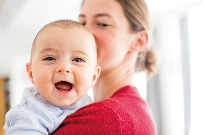 Foto: Ein Kleinstkind blickt mit strahlendem Lachen über die Schulter seiner Mutter.