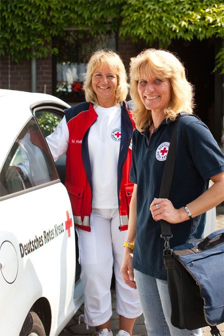 Foto: Zwei hauswirtschaftliche Hilfen des DRK stehen vor einem Dienstfahrzeug. Beide Frauen lachen und haben eine sehr positive Ausstrahlung.